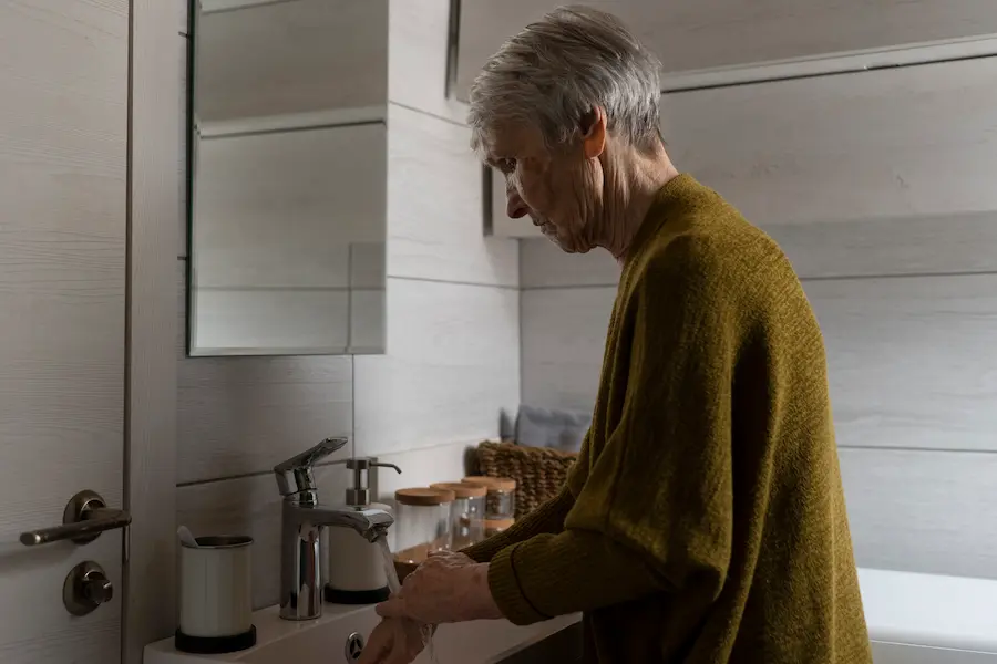 Idosa com dificuldade de equilíbrio em banheiro, representando risco de queda e necessidade de apoio e acessibilidade no dia a dia