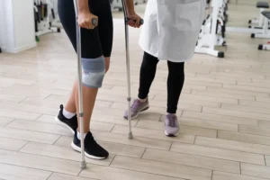 Paciente utilizando muletas e joelheira durante sessão de fisioterapia para recuperação de fratura por estresse.