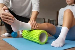 Fisioterapeuta auxilia paciente em exercício de mobilidade com rolo de liberação miofascial.
