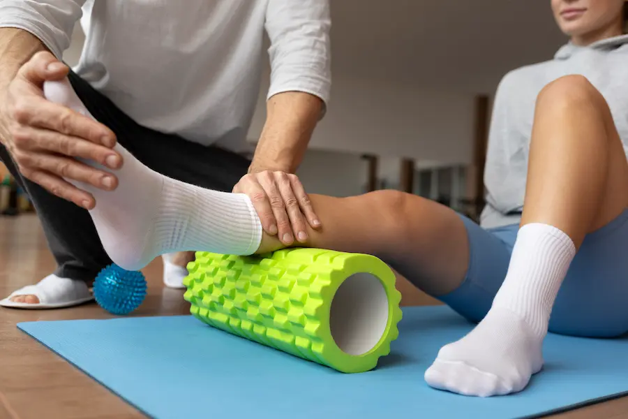 Fisioterapeuta auxilia paciente em exercício de mobilidade com rolo de liberação miofascial.