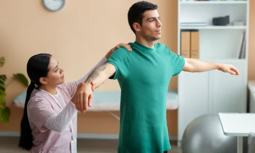 Fisioterapeuta auxiliando paciente em exercício de reabilitação do ombro para recuperação de mobilidade e fortalecimento muscular