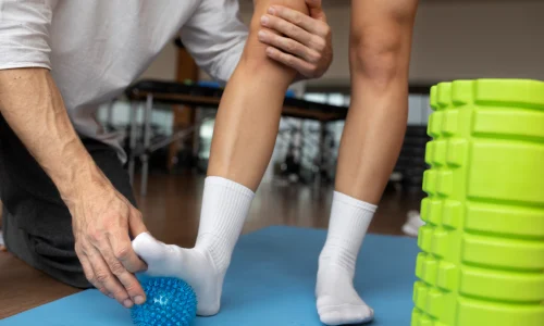 Fisioterapeuta auxiliando paciente em exercício de reabilitação com bola proprioceptiva para fortalecimento e recuperação dos membros inferiores