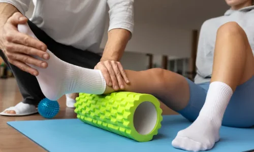 Fisioterapeuta auxilia paciente em exercício de mobilidade com rolo de liberação miofascial.
