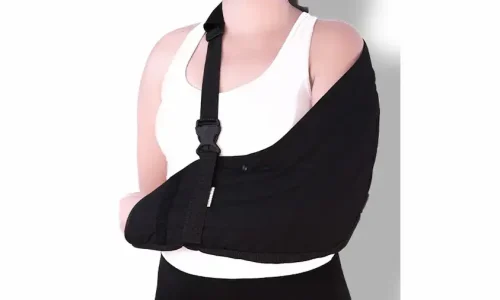 Pessoa utilizando tipoia para ombro preta para imobilização do braço durante tratamento de lesão ou recuperação ortopédica.